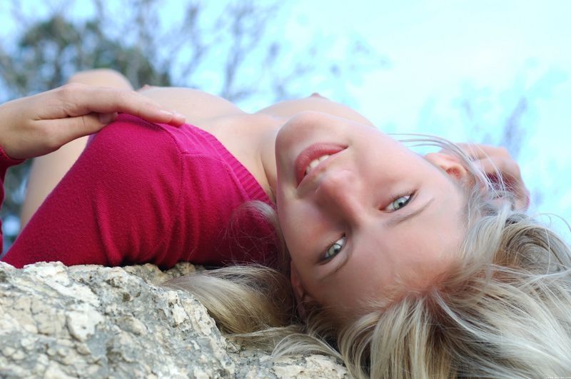 cute young blonde girl posing on rocks in a tight pink sweater