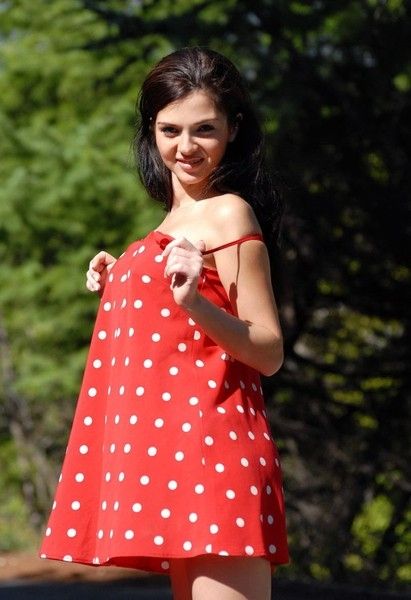 young brunette girl reveals in a red dress with white dots outside on the road