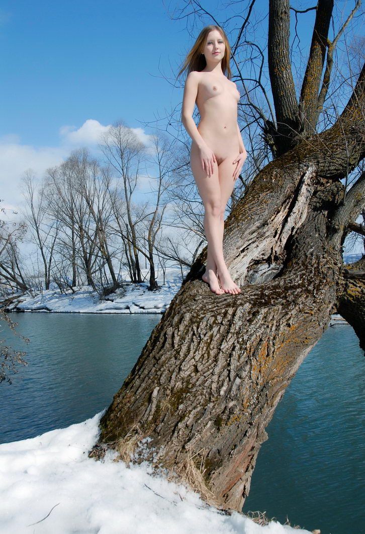 young blonde girl on the tree at the bank of the river in the winter