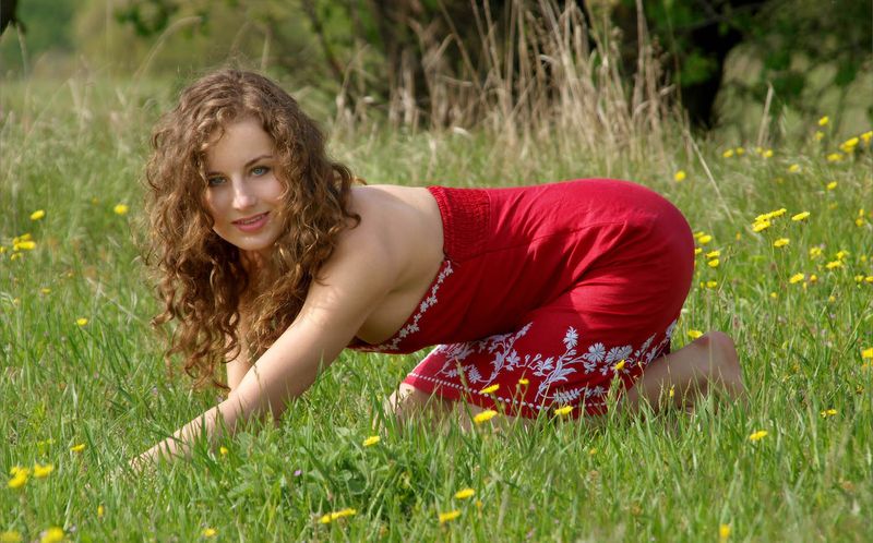 young curly brunette girl strips her red dress on the field of wild flowers