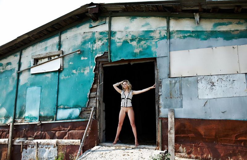 young blonde girl strips her white top near the old building construction