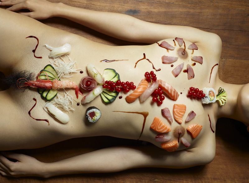 two asian japanese girls practicing a nyotaimori and serving sushi on a naked woman's body
