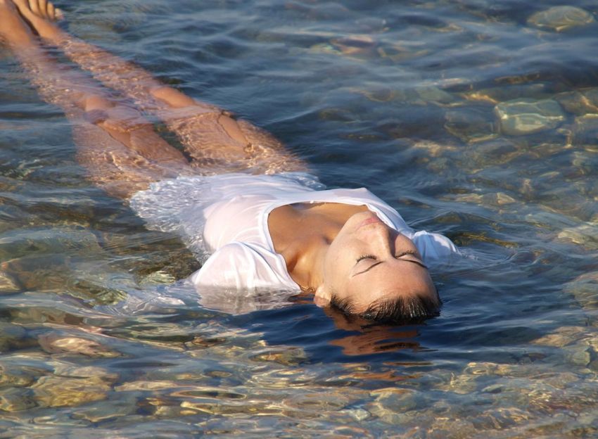 black haired girl undresses her white wet shirt in the sea