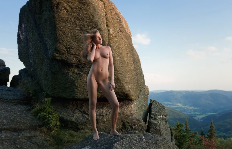cute young blonde girl with a navel piercing posing naked on rocks in high mountains