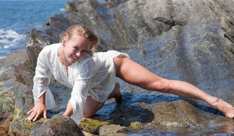young blonde girl undresses her white blouse on the rocky shore at the sea