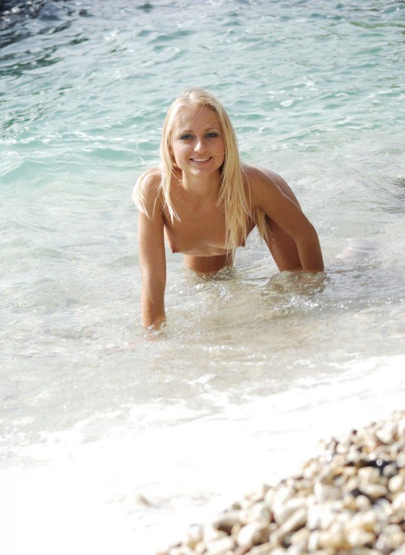 young blonde girl reveals her white fishnet knee highs in the sea on the rocky beach