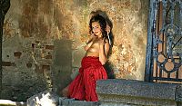 Babes: young curly brunette girl reveals in a red dress at the stone building entrance