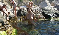 Babes: young brunette girl naturist undresses her sport undershirt and blue shorts in the sea on the public rocky beach