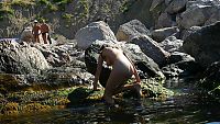 Babes: young brunette girl naturist undresses her sport undershirt and blue shorts in the sea on the public rocky beach
