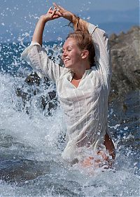 Babes: young blonde girl undresses her white blouse on the rocky shore at the sea