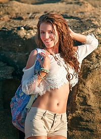 Babes: young curly red haired girl with a necklace reveals her white top and short jeans on the rocky shore at the sea
